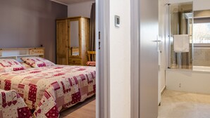 Ein Schlafzimmer mit einem Bett, einem Holzschrank, einem Spiegel und einem Badezimmer mit Dusche und Handtuchhalter.