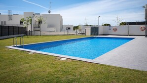 Une piscine rectangulaire à l’eau d’un bleu limpide, entourée d’une terrasse en béton et d’une zone herbeuse.