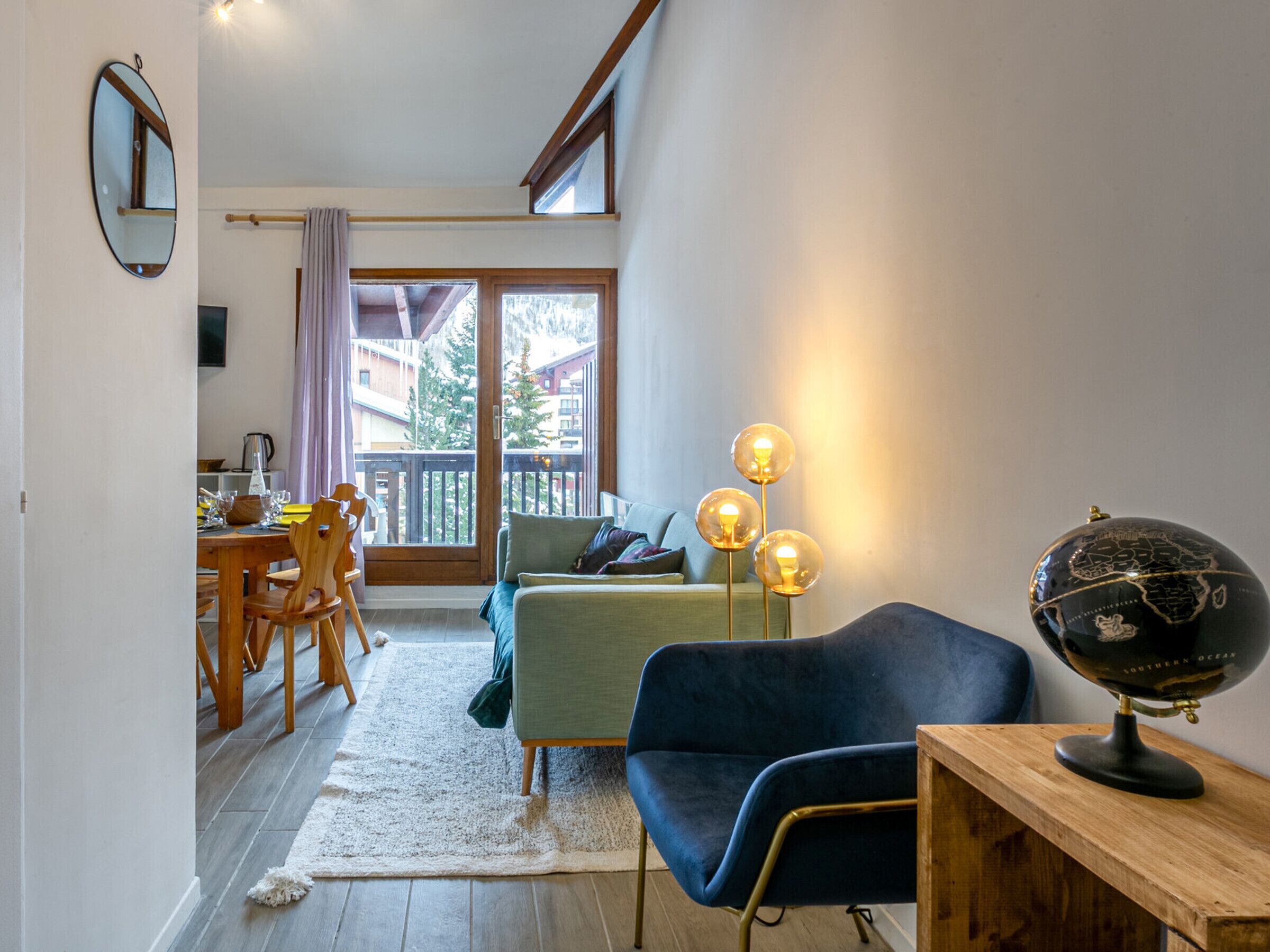 Ein modernes Wohnzimmer mit Essbereich, einem Globus auf einem Holztisch und einem Balkon mit Blick auf Gebäude und Bäume.