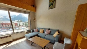 Una sala de estar moderna con un ventanal grande, un sofá gris, una mesa de centro de madera y un sillón gris.