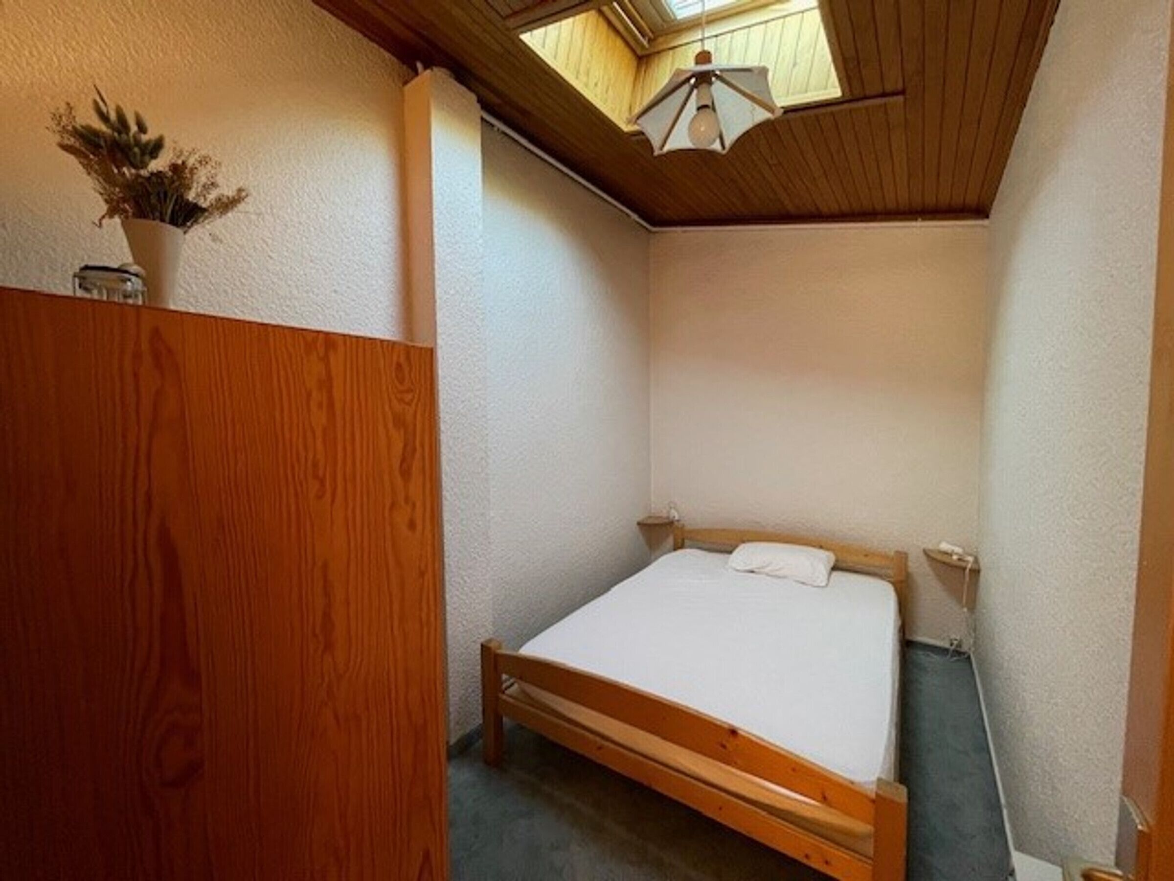Une petite chambre avec un lit simple, un plafond en pente et un puits de lumière.