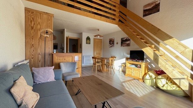 Amplia sala de estar con escalera de madera, sofá, mesa de comedor y zona de cocina.