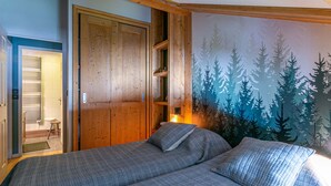 Une chambre avec un grand lit, une armoire en bois et une fresque représentant une forêt sur le mur.