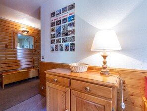A wooden bench and a wall-mounted lamp in a room with a bulletin board displaying photos.