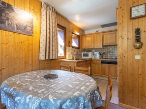 A cozy kitchen with wooden cabinets, a microwave, a sink, and a dining table with a patterned tablecloth.