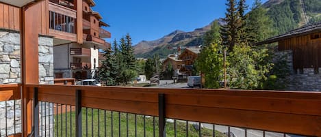 A wooden balcony with a stone wall, overlooking a mountainous landscape with buildings and trees.