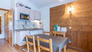 Une cuisine compacte équipée d’un four à micro-ondes, d’un évier et d’une machine à café, une table à manger avec des chaises, et un mur en bois agrémenté d’un luminaire.