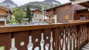 Un chalet en bois aux murs de pierre, doté d’un balcon et offrant une vue sur les montagnes.