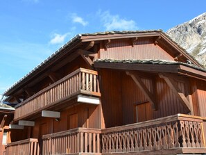Una cabaña de madera tradicional con balcón, techo a dos aguas pronunciado y montañas al fondo.