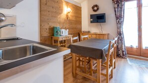 Une cuisine compacte équipée d’un évier, de meubles en bois, d’une table, de chaises et d’un téléviseur fixé au mur.