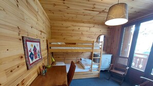 Habitació d'un xalet acollidor amb un llit superposat, un escriptori de fusta amb cadires, una taula petita i una làmpada penjant.