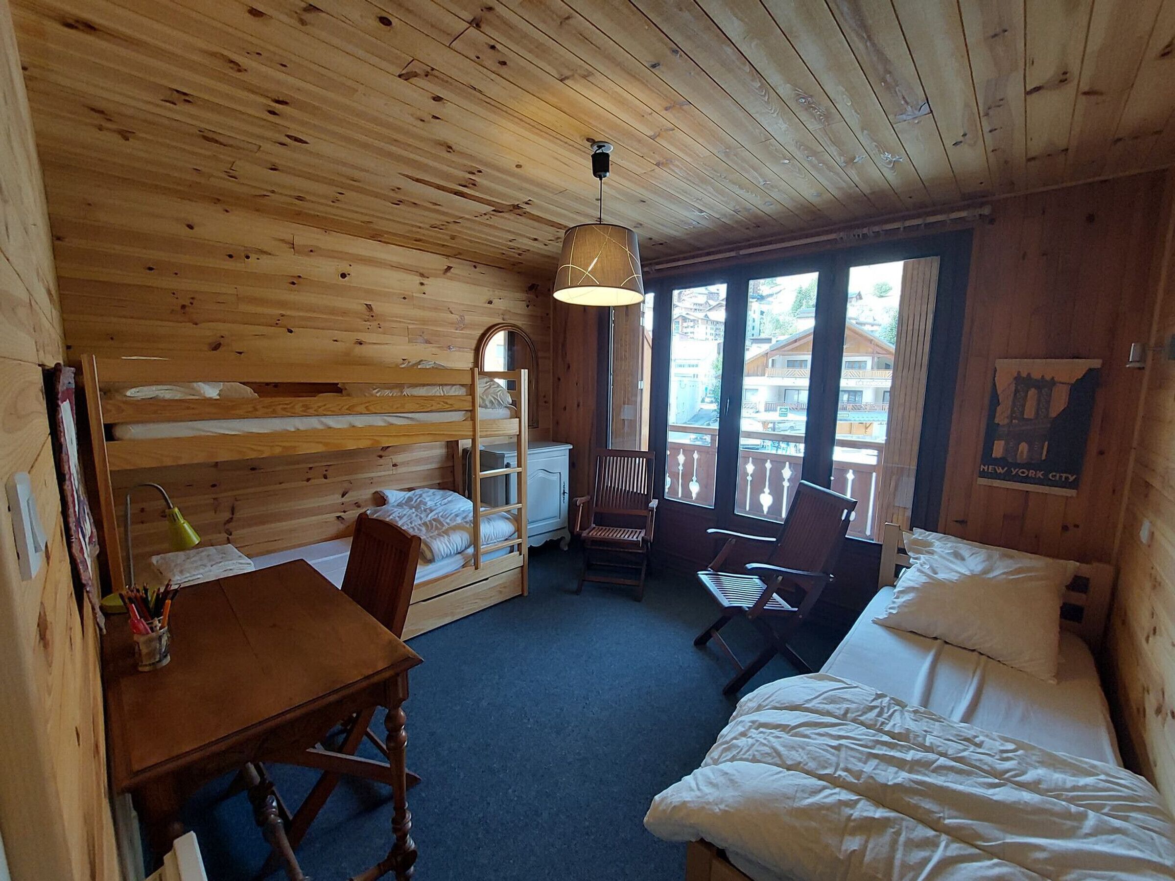 A wooden cabin room with bunk beds, a desk, chairs, and a bed.