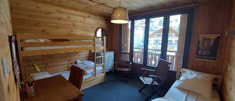 A wooden cabin room with bunk beds, a desk, chairs, and a bed.