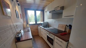 Cuina compacta amb sostre de fusta, una finestra amb cortines, fornet encastrat i un rentapeus.