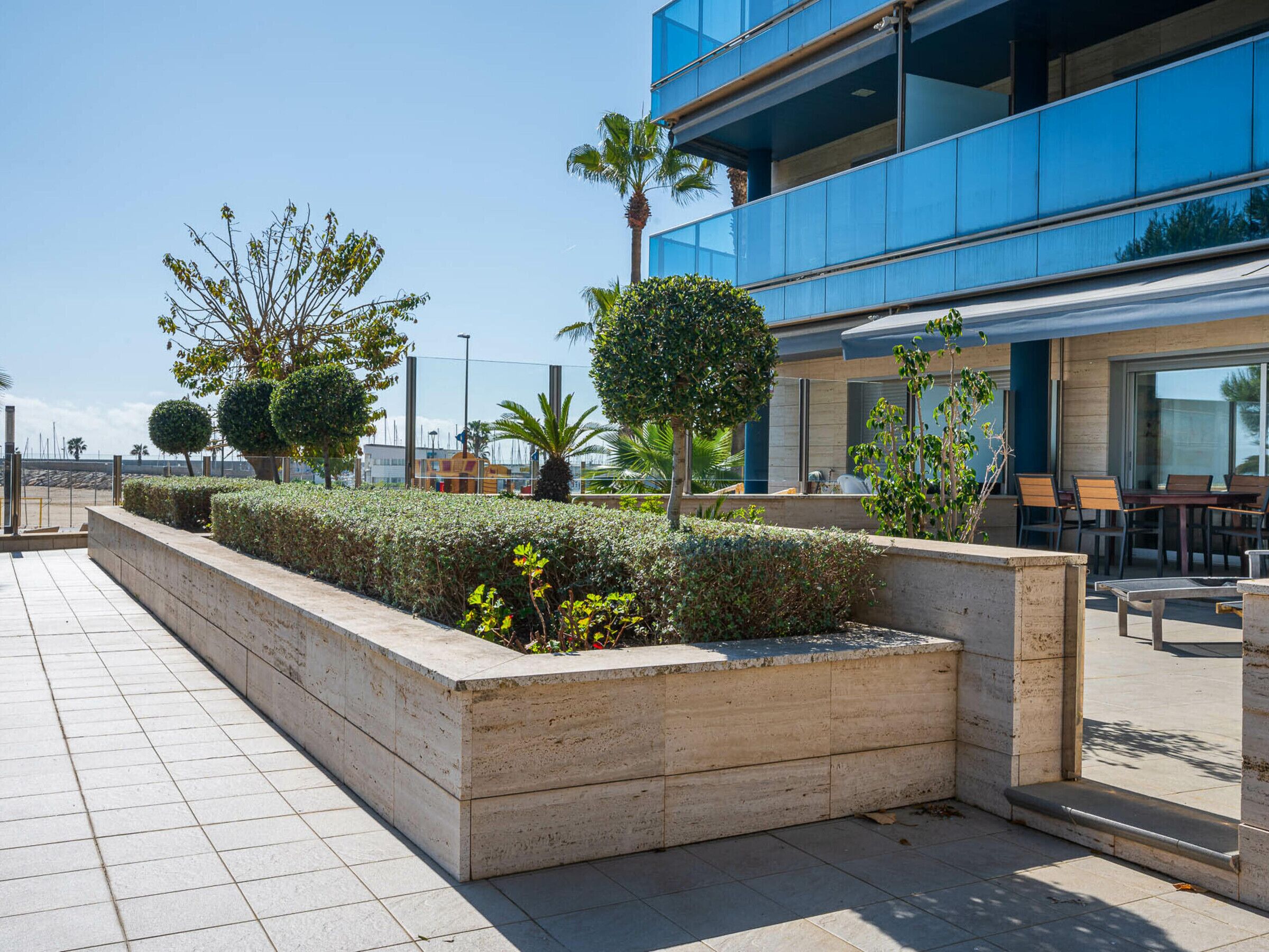 A modern building with a blue facade, a landscaped area with neatly trimmed bushes and trees, and outdoor seating.