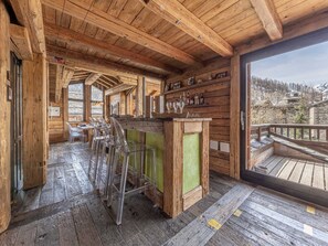 A wooden interior with a bar area, clear chairs, and a view of a snowy landscape.