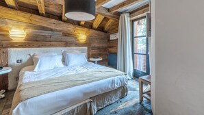 A wooden cabin bedroom with a bed, two bedside tables, a hanging light fixture, and a window with curtains.