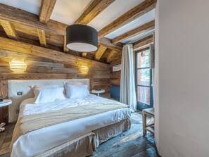 A wooden cabin bedroom with a bed, two bedside tables, a hanging light fixture, and a window with curtains.