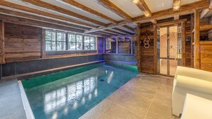 An indoor swimming pool with wooden beams and a glass door.
