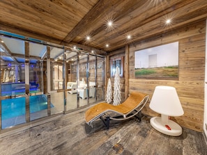 A modern interior with wooden walls, a glass pool, and a lounge area with a white lamp.
