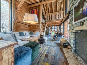 L’intérieur d’un chalet rustique, avec un plafond en bois, des murs en pierre, une cheminée et un coin salon confortable.