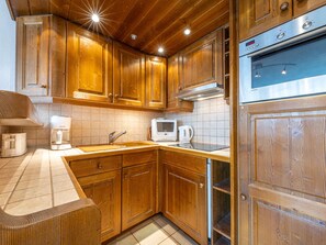 A kitchen with wooden cabinets, a stainless steel oven, a microwave, and a coffee maker. - Elegant and Comfortable Apartment in the Heart of Val-d'Isère (Val-d'Isère)