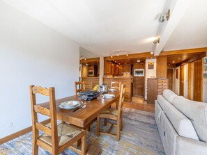 A dining area with a wooden table and chairs, a kitchen in the background, and a sofa in the foreground. - Elegant and Comfortable Apartment in the Heart of Val-d'Isère (Val-d'Isère)