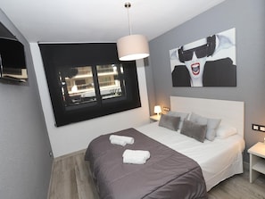 Una habitación de hotel moderna con una cama grande, una ventana con vista a la ciudad, un televisor de pantalla plana en la pared y un cuadro sobre la cama.