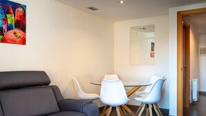 Una sala de estar moderna con un sofá gris, sillas blancas, una mesa de vidrio y un cuadro de colores en la pared.