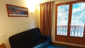 Una stanza con un divano scuro, un tavolino, un quadro appeso al muro e una porta-finestra con vista sugli alberi.