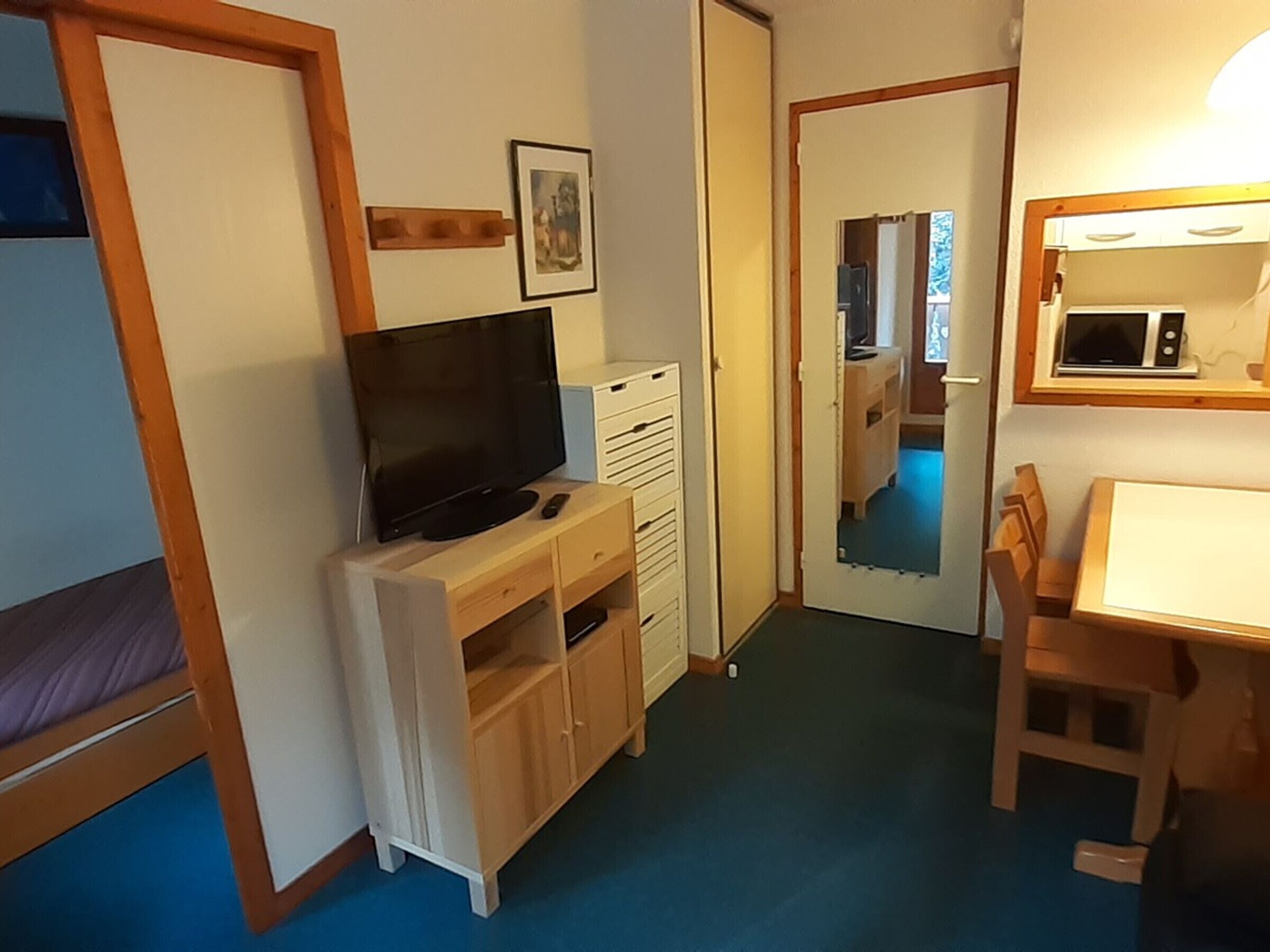 A compact room with a bed, a TV on a wooden stand, a small table, and a microwave.