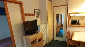 Una stanza compatta con un letto, una TV su un mobiletto in legno, un tavolino e un forno a microonde.