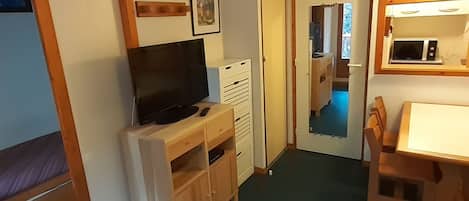 A compact room with a bed, a TV on a wooden stand, a small table, and a microwave.