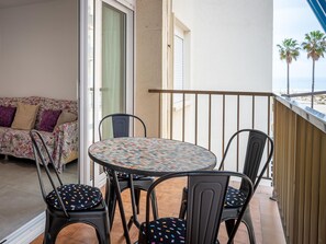 Un balcón con una mesa redonda y cuatro sillas, un sofá con cojines estampados y vista a la playa.