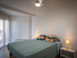 Un dormitorio con una cama, dos mesitas de noche, un ventilador de techo y una ventana con cortinas.