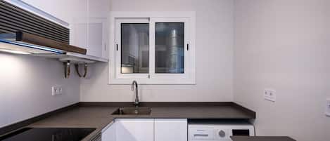 Cocina compacta con lavadora y secadora integradas, una ventana y un lavamanos de acero inoxidable.