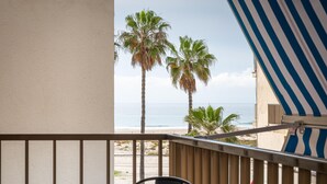 A balcony with a view of the beach, palm trees, and a striped awning. - Bright apartment sea view - 4 guests (Torredembarra)