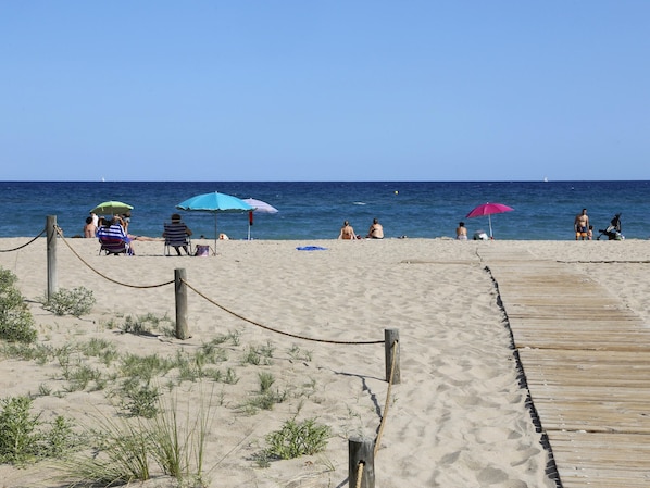 A sandy beach with a wooden boardwalk leading to the water, a rope barrier, and beach umbrellas.