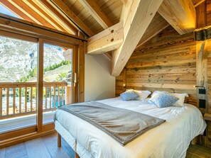 A bedroom with a wooden ceiling, a large bed with pillows, and a sliding glass door leading to an outdoor area.