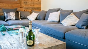 Un accogliente soggiorno con parete in legno, un divano blu e un tavolo con una bottiglia di champagne Ruinart e un gioco Scrabble.