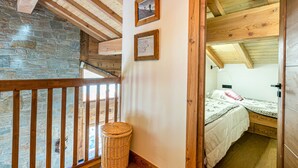 Un balcone in legno con un muro in pietra, un cesto di vimini e un letto con copripiumino bianco.