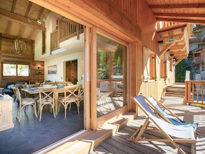 A wooden cabin with a dining area, lounge chairs, and a deck.