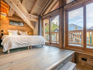 A bedroom with a bed, wooden walls, large windows, and a view of mountains.
