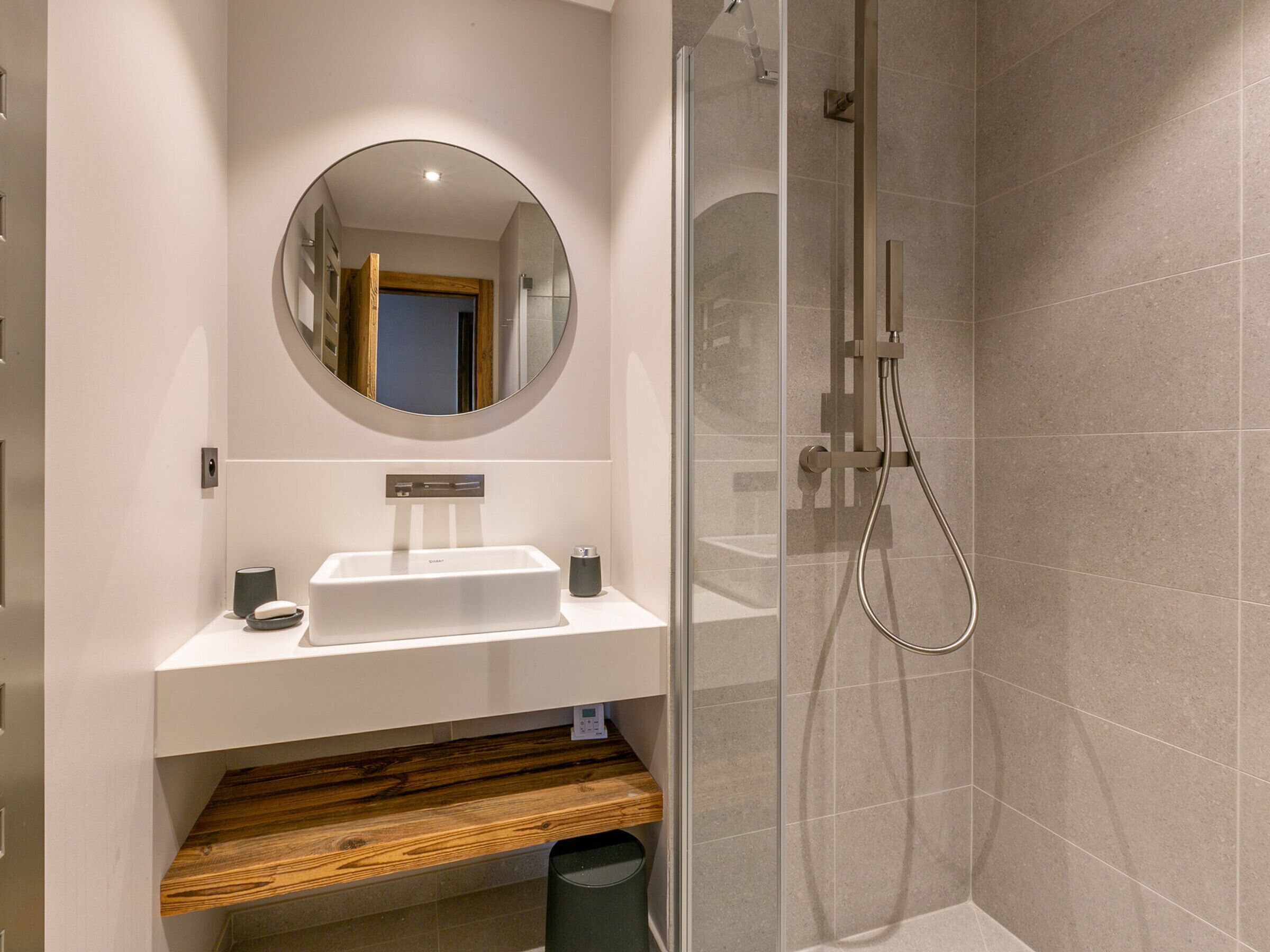 Une salle de bain moderne avec une douche à l’italienne en verre, un lavabo blanc et une étagère en bois.