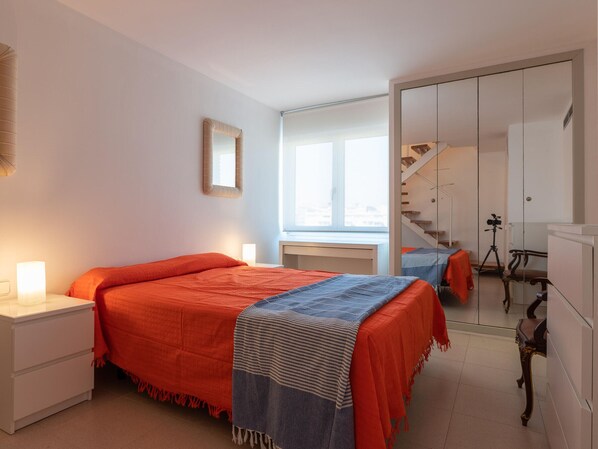 Un dormitorio con dos camas, una mesita de noche, un espejo, una ventana y una escalera.