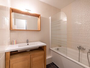 A bathroom with a white sink, wooden cabinet, and a glass-enclosed shower area. - Charming Apartment with Full Amenities, Wifi, Parking, and South-Facing Balcony in Val-d'Isère (Val-d'Isère)