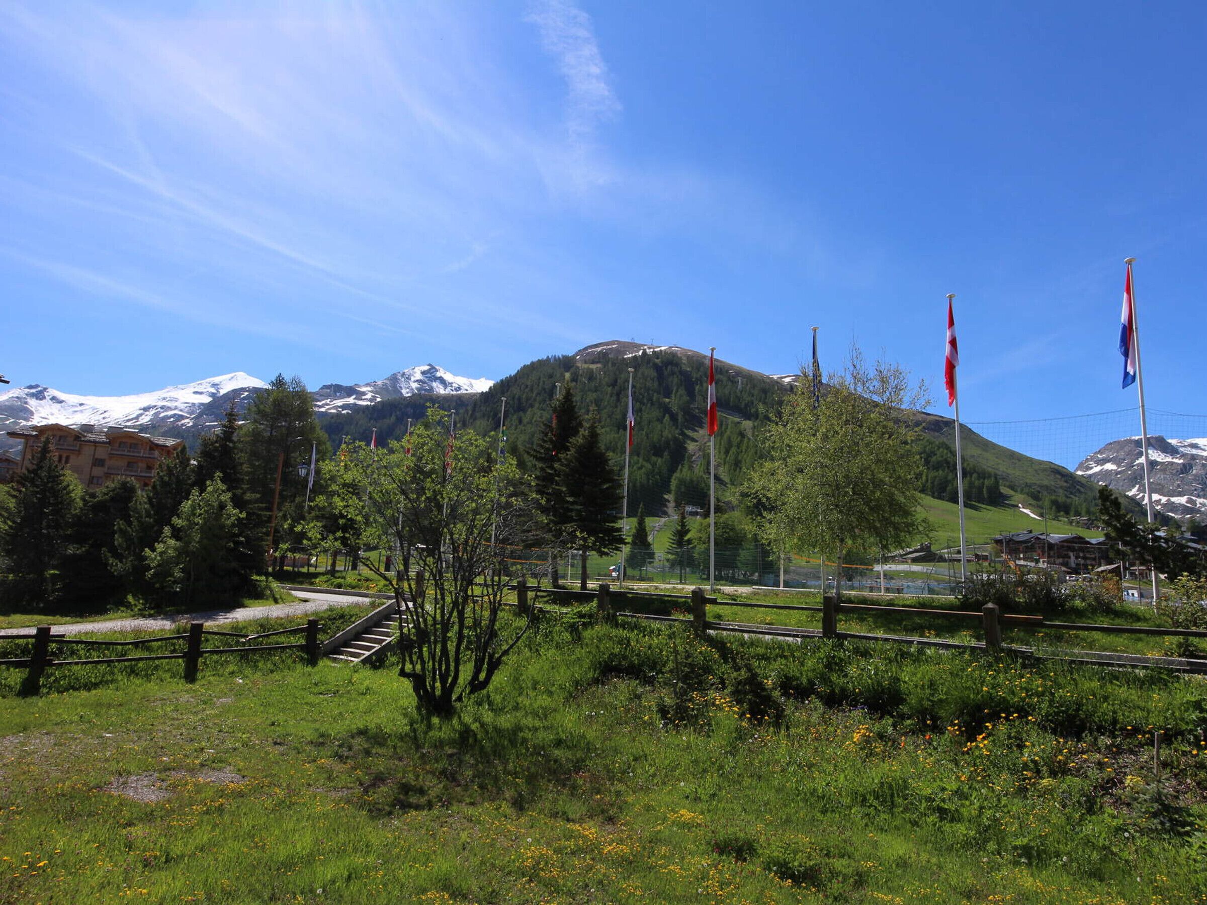 A mountainous landscape with a clear sky, a wooden fence, and several flags.