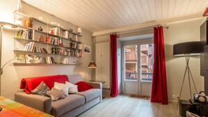 A cozy living room with a sofa, a bookshelf, a window with red curtains, and a floor lamp.