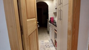 A narrow hallway leading to a kitchen with wooden cabinets and a tiled floor.