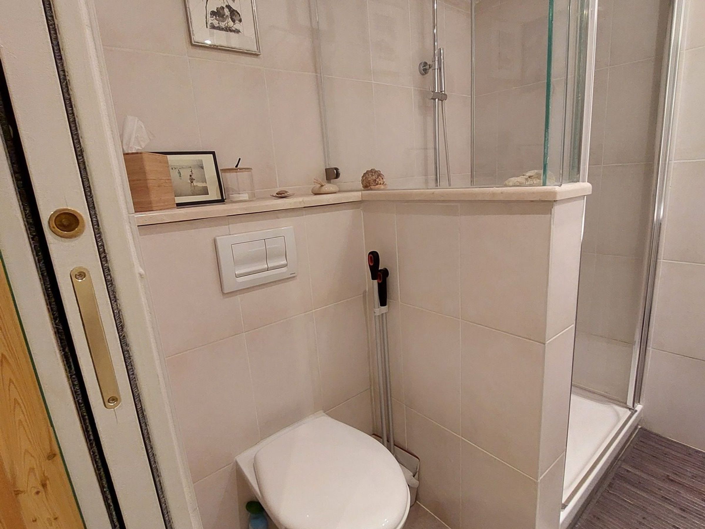 Een kleine, compacte badkamer met toilet, douche en een douchecabine met glazen wanden.